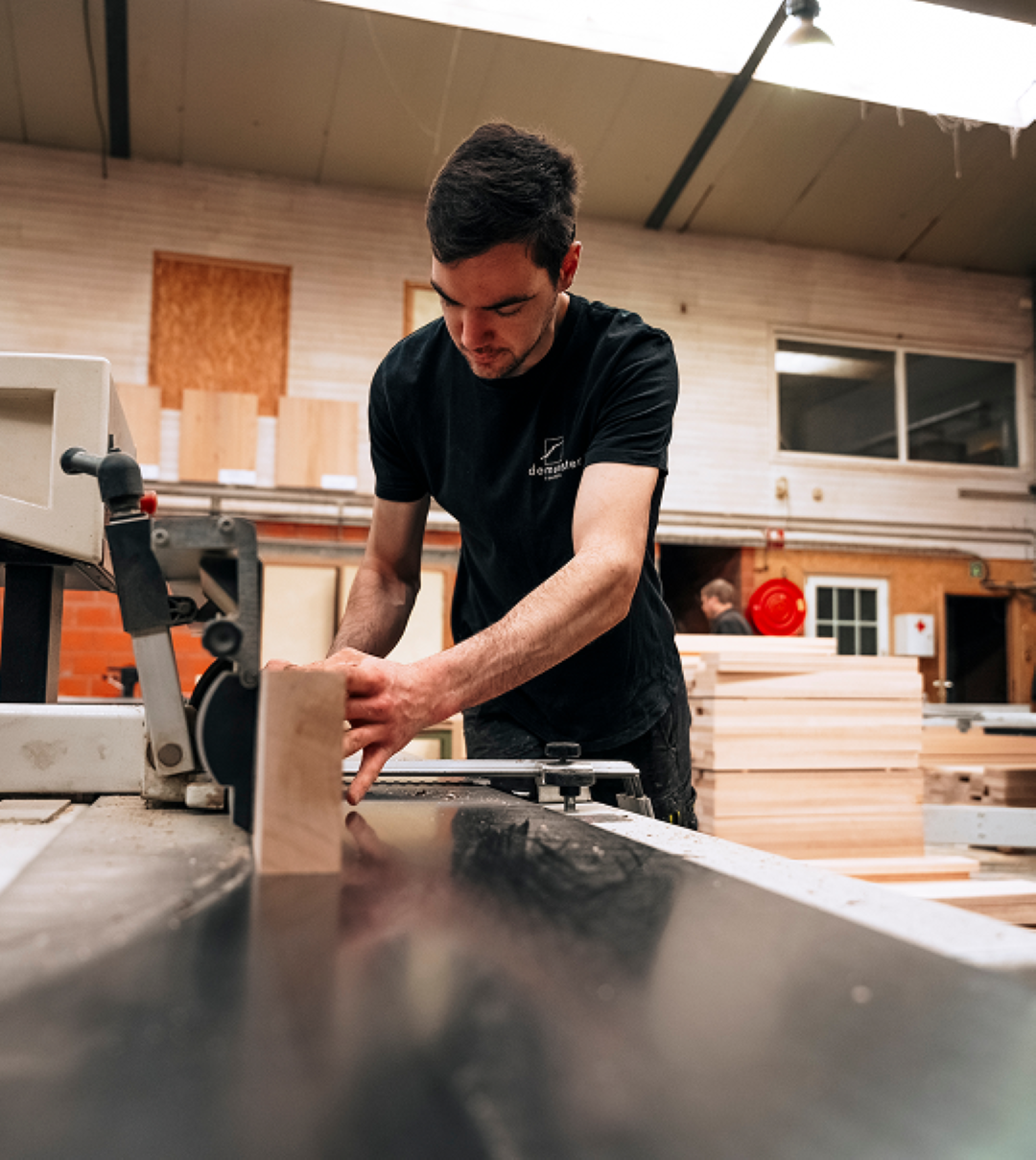 Man in een houtatelier die geconcentreerd een stuk hout bewerkt met een cirkelzaagmachine.